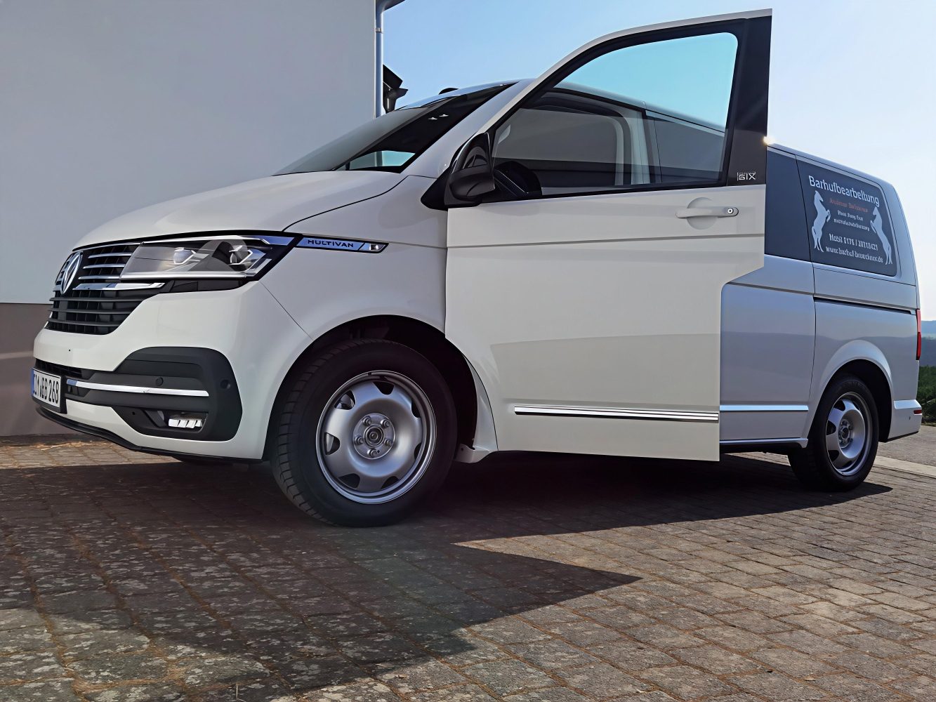 Mobil unterwegs - zuverlässig geplant Ein weißer VW Multivan mit offener Fahrertür und der Aufschrift "Barhufbearbeitung" auf der Schiebetür.